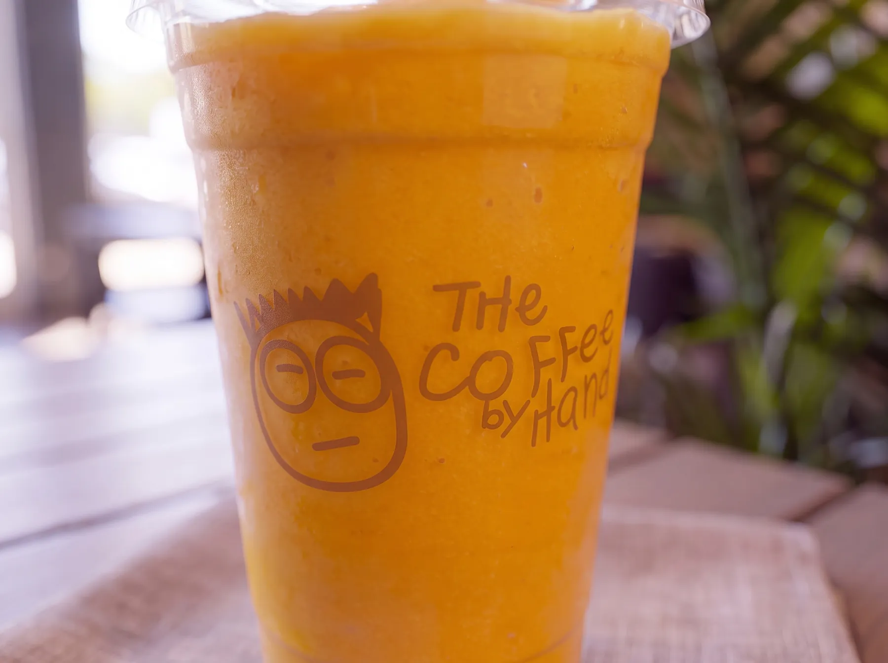 A mango smoothie in a branded Coffee By Hand cup.